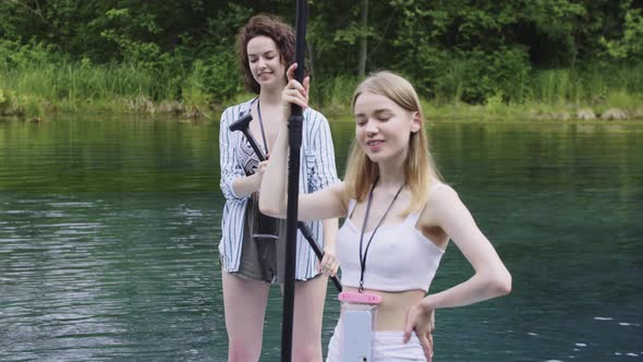 Two Young Happy Women Standing on Boards in the River and Looking in the Camera