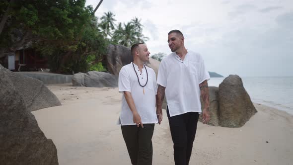 Lovely Married Gay Couple Honeymooners Walking Holding Hands Along the Rocky Beach By the Sea and