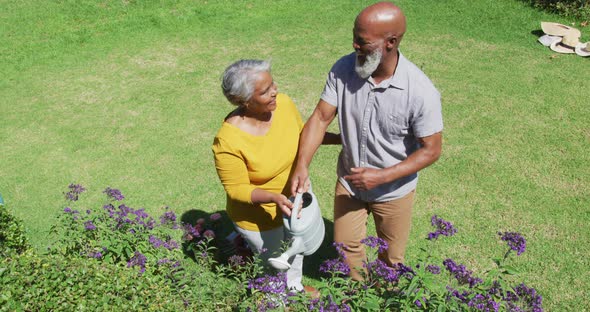 African american senior couple smiling while watering plants together in the garden