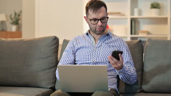 Attractive Man with Laptop Using Smartphone 