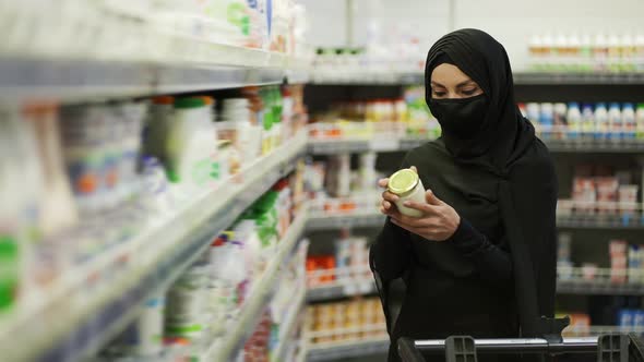 Woman in Hijab and Protective Mask Doing Shopping Takes Product From the Shelf in a Milk Section