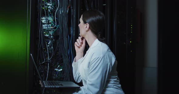 Caucasian female it technician in lab coat using laptop checking computer server