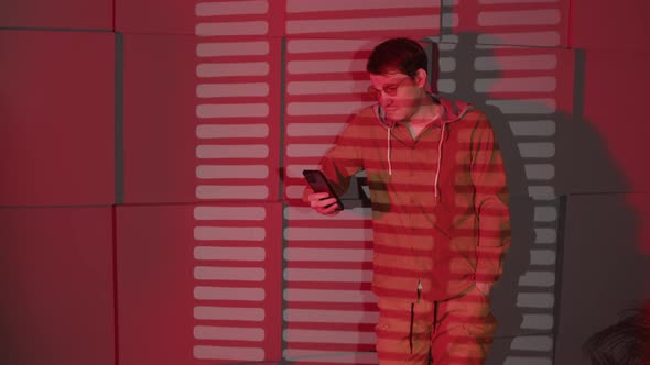 Man in Glasses Browsing Mobile Phone Standing Near Wall with Shadows of Jalousie and Space for Text