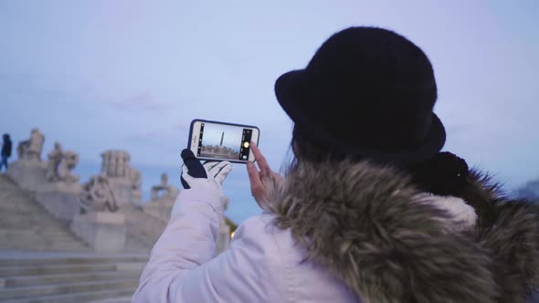 Back view of Asian woman standing and taking a photo in public Frogner park, Norway