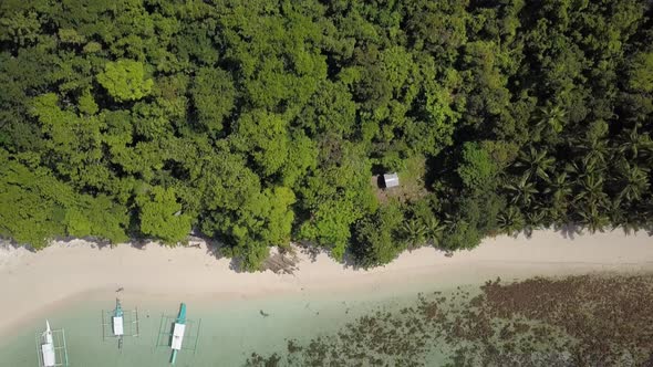 Aerial backwards tracking shot from green tropical island with vegetation to sandy beach with crysta