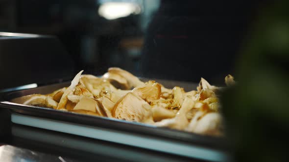 Restaurant kitchen, close-up: oils are added to mushrooms before frying in professional kitchen