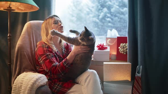 Smiling Beautiful Blonde Woman Playing with Grey Domestic Cat Sitting at Window