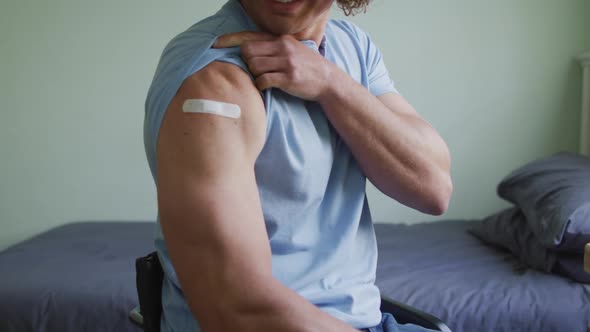 Midsection of caucasian disabled man in wheelchair showing bandage on arm after covid vaccination