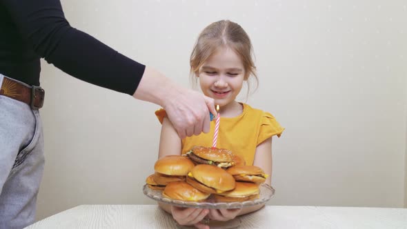 a Funny Little Girl Makes a Wish and Blows Out a Candle on a Hamburger Cake