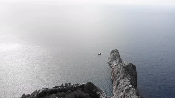 Huge stony cliff in blue ocean with boat sailing near