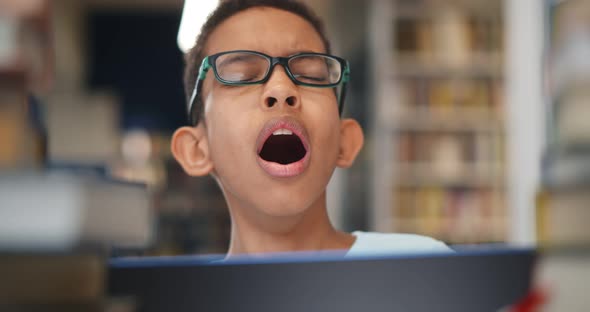 Portrait of Sleepy Hard Working Schoolboy Sitting at Library and Yawning Using Laptop