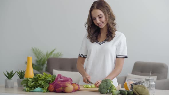 Young Skill Cute Woman Slicing Vegetables with the Sharp Knife at the Table in the Kitchen