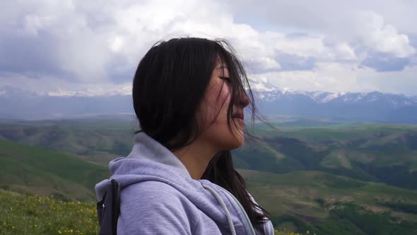 Young Asian Girl Stand on a Windy Field in the Mountains and Straightens Her Hair