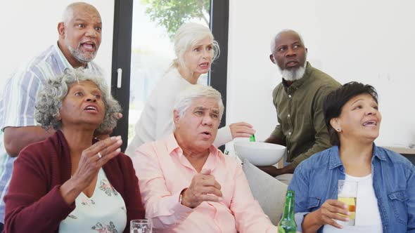 Happy senior diverse people watching tv with beer at retirement home