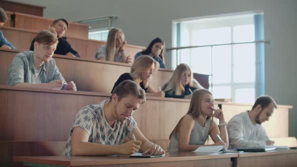 Modern Students Men and Women Sit at Desks in a Large Classroom and Write a Lecture Notes