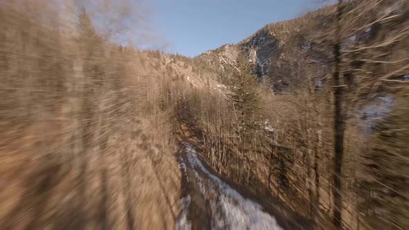 fpv drone flying along a forest road up to the austrian mountains with a frozen waterfall at sunset