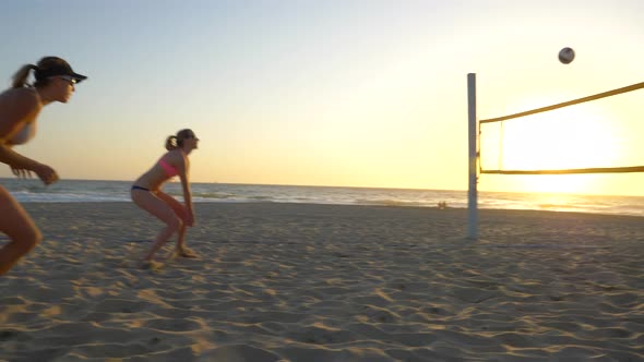Women teams play beach volleyball at sunset and a player passes the ball.