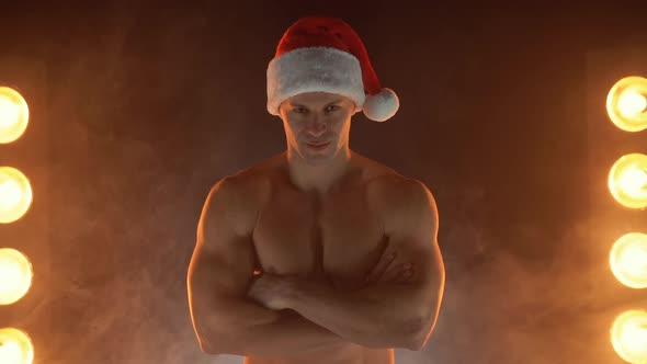 Portrait of Muscular Man Wearing Christmas Santa Hat Standing on Smoky Background