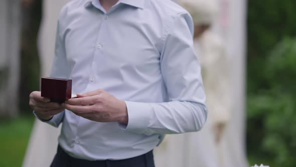 Unrecognizable Young Caucasian Man Holding Ring Box in Hands with Blurred Middle Eastern Woman