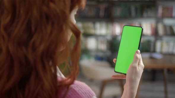 Back View of Redhead Woman Holding Chroma Key Green Screen Smartphone Watching Content With Touching alt