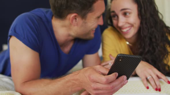 Happy caucasian couple lying on bed and using smartphone