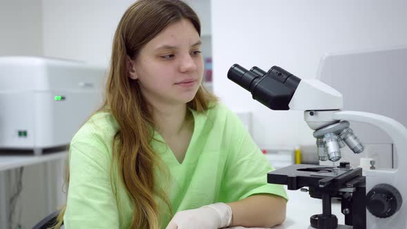 Portrait of Expert Young Lab Assistant Posing at Microscope Indoors Smiling