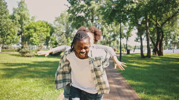 Man Circles His Daughter Sitting on His Piggyback While Walking in a City Park