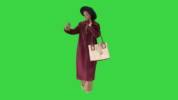 Beautiful African American Fashion Girl in Coat and Black Hat Texting on Her Phone While Walking on