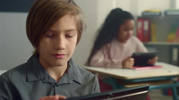 Smiling Schoolboy Sitting at Desk with Digital Tablet in Elementary School