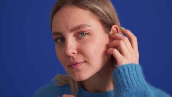 Smiling woman wearing blue sweater correcting her appearance at the camera