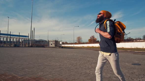 Young Handsome Brutal Bearded Man Running with a Backpack, Autumn Day, Funny Style