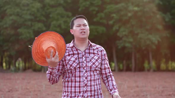 Asian adult standing serious farmer man tired take off hat on cultivated area