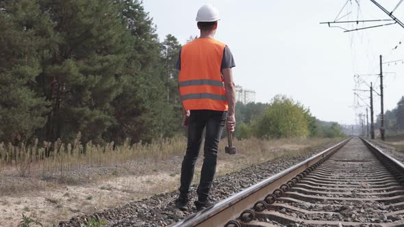 The railwayman stands along the tracks, a working sledgehammer in his hand.