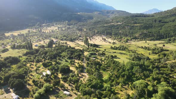 Pan left flying above El Hoyo valley surrounded by a beautiful woodland and mountains in background,