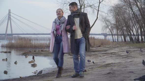 Portrait of Adult Caucasian Couple Walking Along Riverbank and Leaving. Ducks Flying Up From the