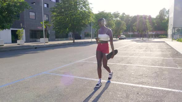 Slow motion shot of young woman with skateboard walking in city