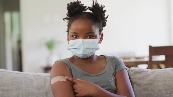 African american girl wearing face mask pointing at bandage on her arm