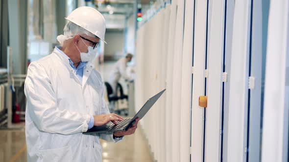 Factory Worker is Observing Equipment While Typing on a Laptop