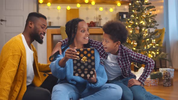 Young African Woman Opening Present From Husband and Son on Christmas Eve