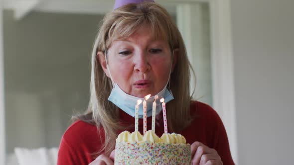 Senior Caucasian woman spending time at home, sitting in her living room blowing candles on birthday