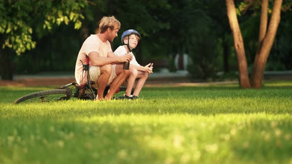 A positive father is sitting with his son and talking on the grass