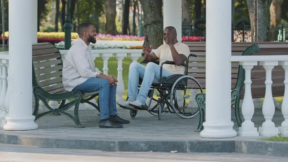 Mature Black Man and His Young African Male Friend Sitting Outdoors Talking Discussing Perspectives