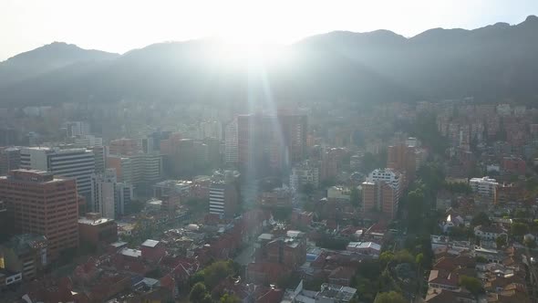Aerial - Rising drone shot of Chapinero, Bogota, Colombia, with mountain background and sunflares