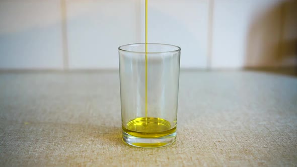 Cooking oil being drizzledinto glass on kitchen bench.