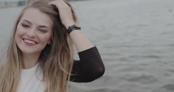 Girl Smilling Into Camera and Correcting Her Blowing Hair at River Background