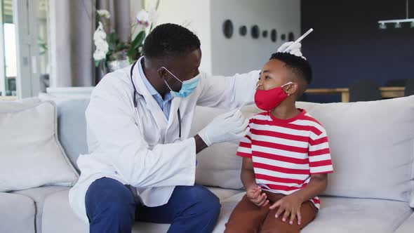 African american doctor wearing face mask taking a nasal swab sample of boy at home