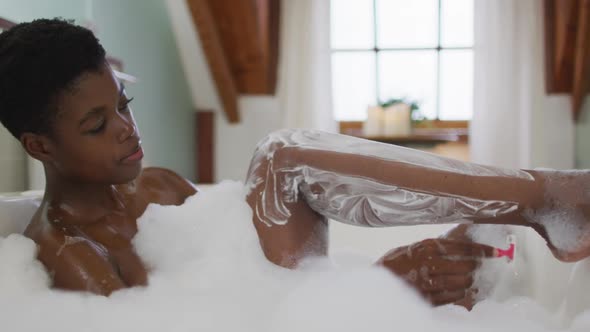 African american attractive woman shaving legs in foam bath in bathroom