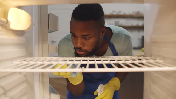 View From Inside Empty Refrigerator African Man Wearing Rubber Gloves Cleaning Shelves