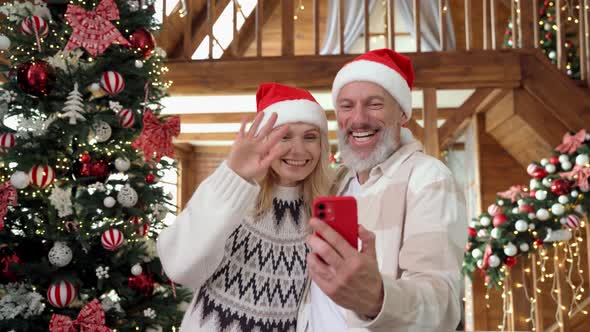 Happy Mature Couple in Santa Hats Greeting Family on Phone Christmas Video Call