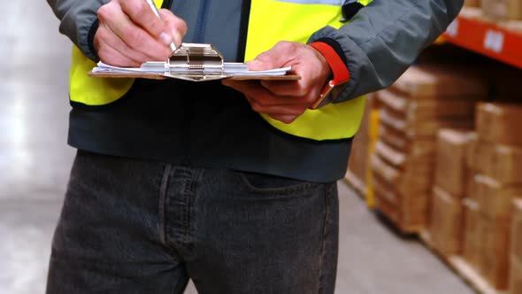 Mid section of warehouse worker writing on clipboard